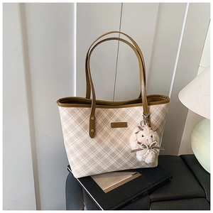 Detail of beige plaid tote bag with brown straps and white plush rabbit charm