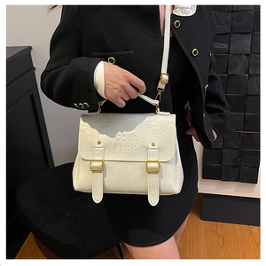 Detail of white wrinkled faux leather bag featuring top handle and gold metal hardware