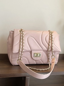 Quilted light pink chain crossbody bag with golden metal lock on dark wood surface