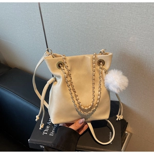 Détail d'un sac seau crème avec chaîne dorée et pendentif pompon en peluche blanc