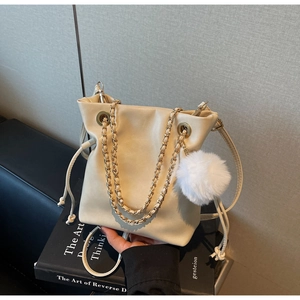 Détail du sac seau beige avec cordon de serrage, chaîne dorée et pompon en fourrure