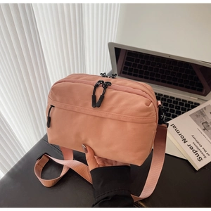 Close-up of pink nylon crossbody bag with multi-zipper compartments and wide strap