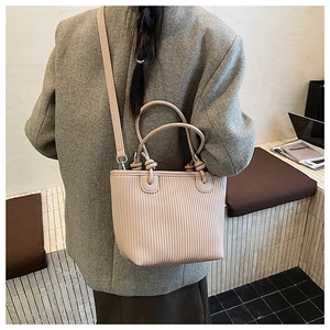 Detail of apricot woven shoulder bag with knotted handle and pleated texture on grey suit
