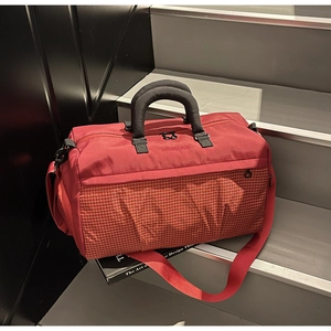 Close-up of a large red canvas travel bag with white checkered pattern on a grey step