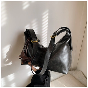 Detail of vintage black leather underarm bag featuring horse pendant and brass buckle hardware