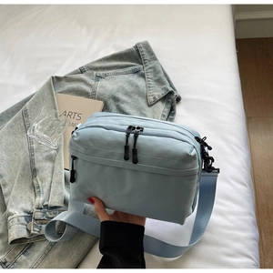 Close-up of light blue crossbody bag featuring three zipper pockets and durable nylon strap