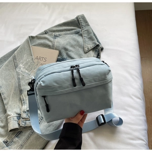 Close-up of a light blue nylon crossbody bag with dual zippers and adjustable strap