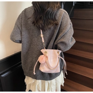 Détail du sac seau rose à cordon avec breloque pelucheuse et chaîne sur pull en maille