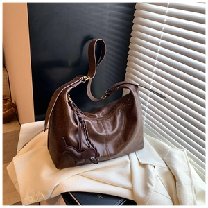Detail view of large brown leather hobo bag with a dog-shaped charm on white blazer