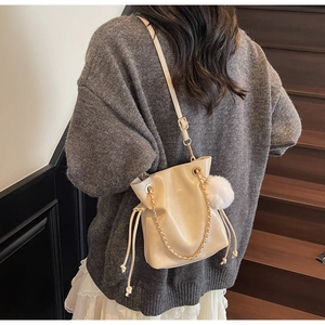 Detail of cream drawstring bucket bag featuring shiny leather and gold chain strap