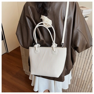 White pleated leather bucket bag shown on person wearing a brown vintage leather jacket