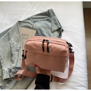 Detailed view of pink nylon crossbody bag with three zipper compartments on white bedding
