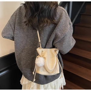 Detail view of cream drawstring bucket bag with gold chain and white fur pompom charm