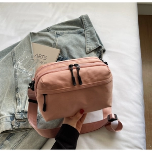 Detail of pink nylon crossbody bag showing multiple zip pockets and adjustable strap