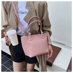 Detailed texture of pink pleated bucket bag held by model in casual beige trench coat