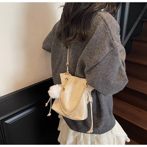 Détail du sac seau beige à cordon avec chaîne dorée et pompon en peluche sur un modèle