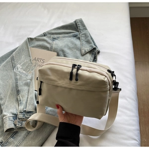 Detail of beige nylon crossbody bag with dual zipper compartments and wide strap