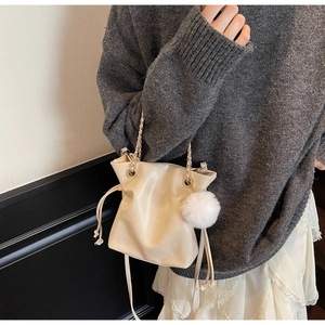 Détail du sac seau en cuir crème avec pompon en peluche et bandoulière chaîne dorée