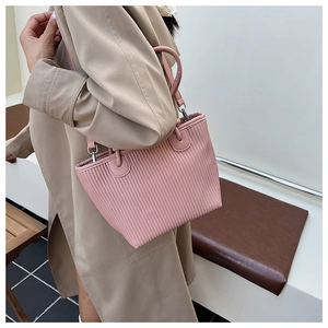 Pink pleated tote bag shown worn as a crossbody by a model in a minimalist interior