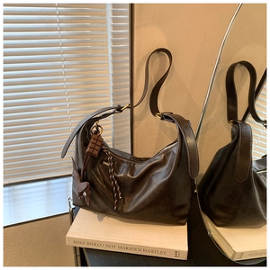 Detail of dark brown glossy leather hobo bag with unique charms on a white book