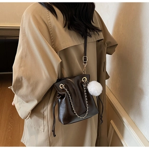 Détail du sac seau marron foncé à cordon avec chaîne dorée et pompon blanc en peluche