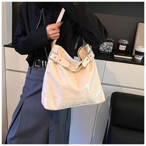Detail view of large beige tote bag featuring silver metal buckles and soft leather texture
