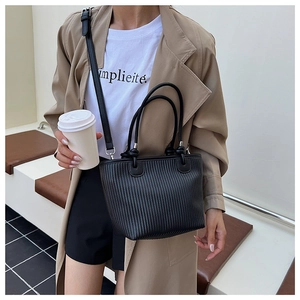 Detail of black woven texture tote bag worn with a stylish trench coat in street style