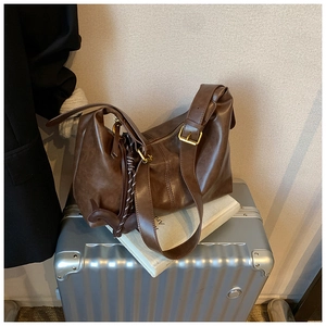Deep brown matte PU leather shoulder bag with adjustable strap on a travel suitcase