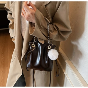 Détail d'un sac seau marron foncé en cuir brillant avec cordon et pompon blanc