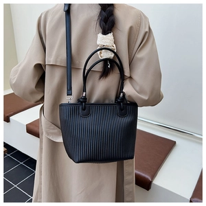 Detailed view of black woven texture tote bag worn by a model in a beige trench coat