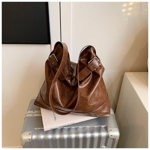 Detail of vintage brown leather tote bag with adjustable metallic buckle on silver suitcase