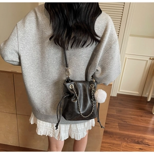 Vue détaillée d'un sac seau noir en similicuir avec chaîne dorée et pompon blanc