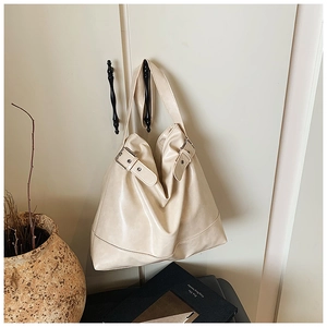 Detail of a cream-colored hobo tote bag featuring metal side buckles and soft wax leather texture