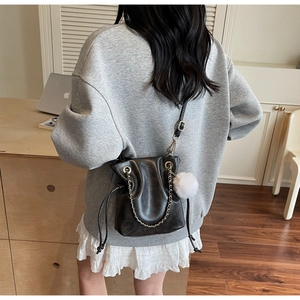 Detail of black drawstring bucket bag with metal chain strap and white plush pompom