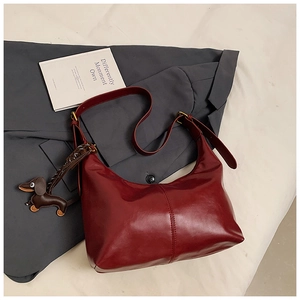 Detail of burgundy leather crescent shoulder bag with dog charm on grey suit