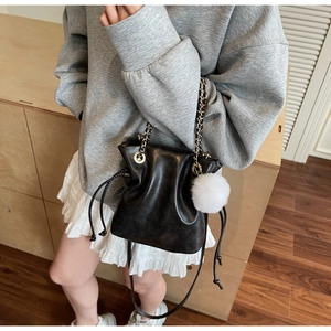 Détail du sac seau noir à cordon avec chaîne dorée et pompon en fausse fourrure