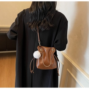 Détail du sac seau en cuir marron avec chaîne dorée et breloque pompon blanc doux