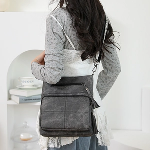 Detailed view of dark grey crossbody bag with double tassels and multi-zipper compartments