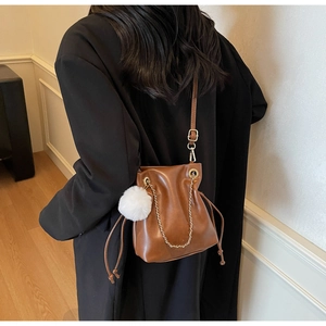 Détail du sac seau en cuir marron foncé avec chaîne dorée et pompon en fourrure blanche