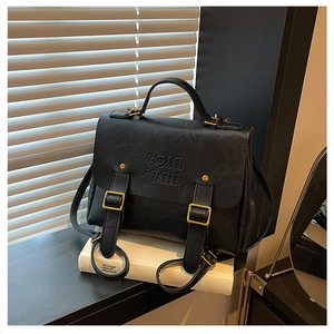 Close-up of matte black leather bag with embossed COIN text and vintage gold metal buckles