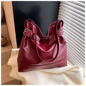 Detail of burgundy leather tote bag with silver buckle straps on a white textile