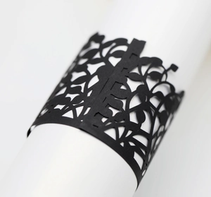 Detail of laser-cut black paper napkin ring with intricate vine and flower hollow pattern