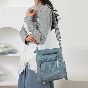 Detail of blue textured crossbody bag with white tassels and geometric woven strap