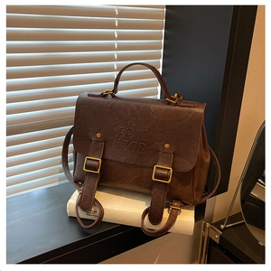 Detail of vintage dark brown faux leather bag with gold buckle on white books