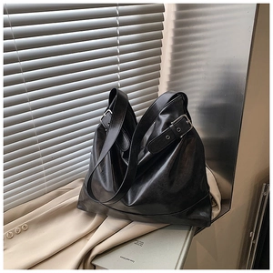 Detail of minimalist black leather tote bag featuring a silver buckle on wide shoulder strap