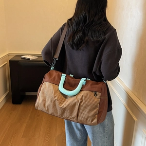 Large travel duffel bag with brown plaid stitching and blue padded handles on shoulder strap