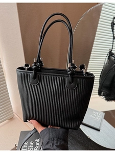 Black pleated tote bag with woven texture and silver hardware in a minimalist style