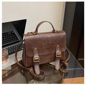 Detail of vintage brown leather backpack with embossed text and gold buckle on a desk