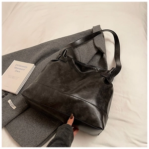 Detailed view of black large capacity tote bag on grey wool coat with matte leather texture
