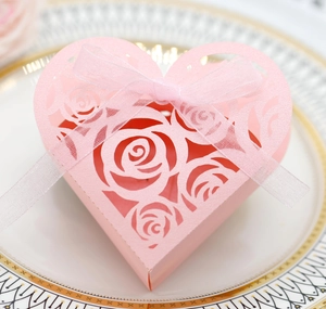 Pink laser-cut heart favor box with rose patterns and ribbon on a porcelain plate